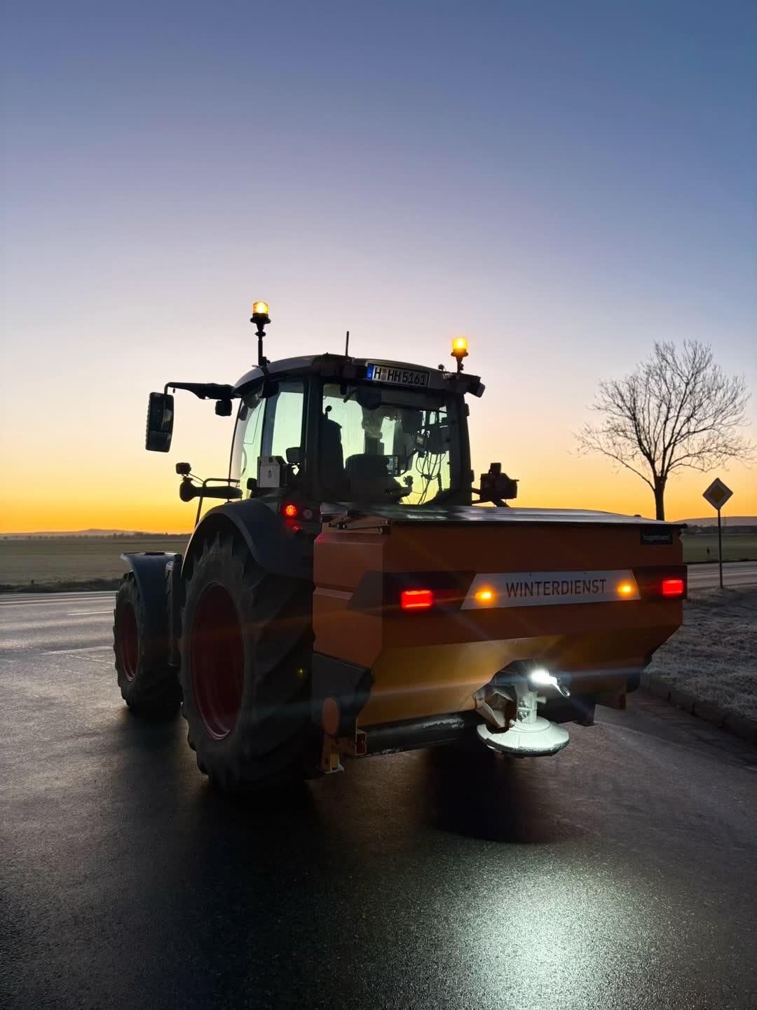 Traktor mit Streuautomat im Winterdienst-Einsatz bei Sonnenaufgang